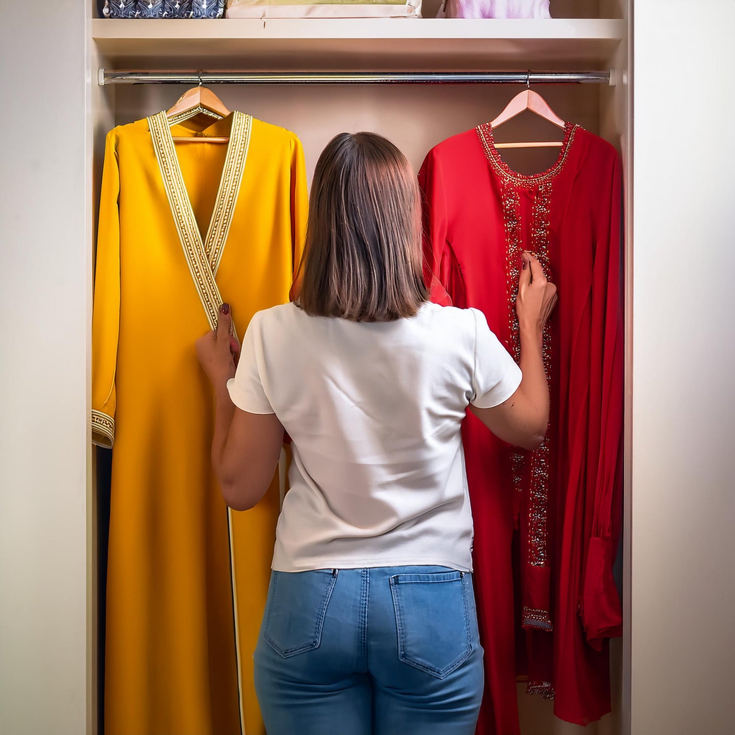 Woman picking between two Pakistani shalwar kameez outfits in her closet. What stays what goes? Decluttering